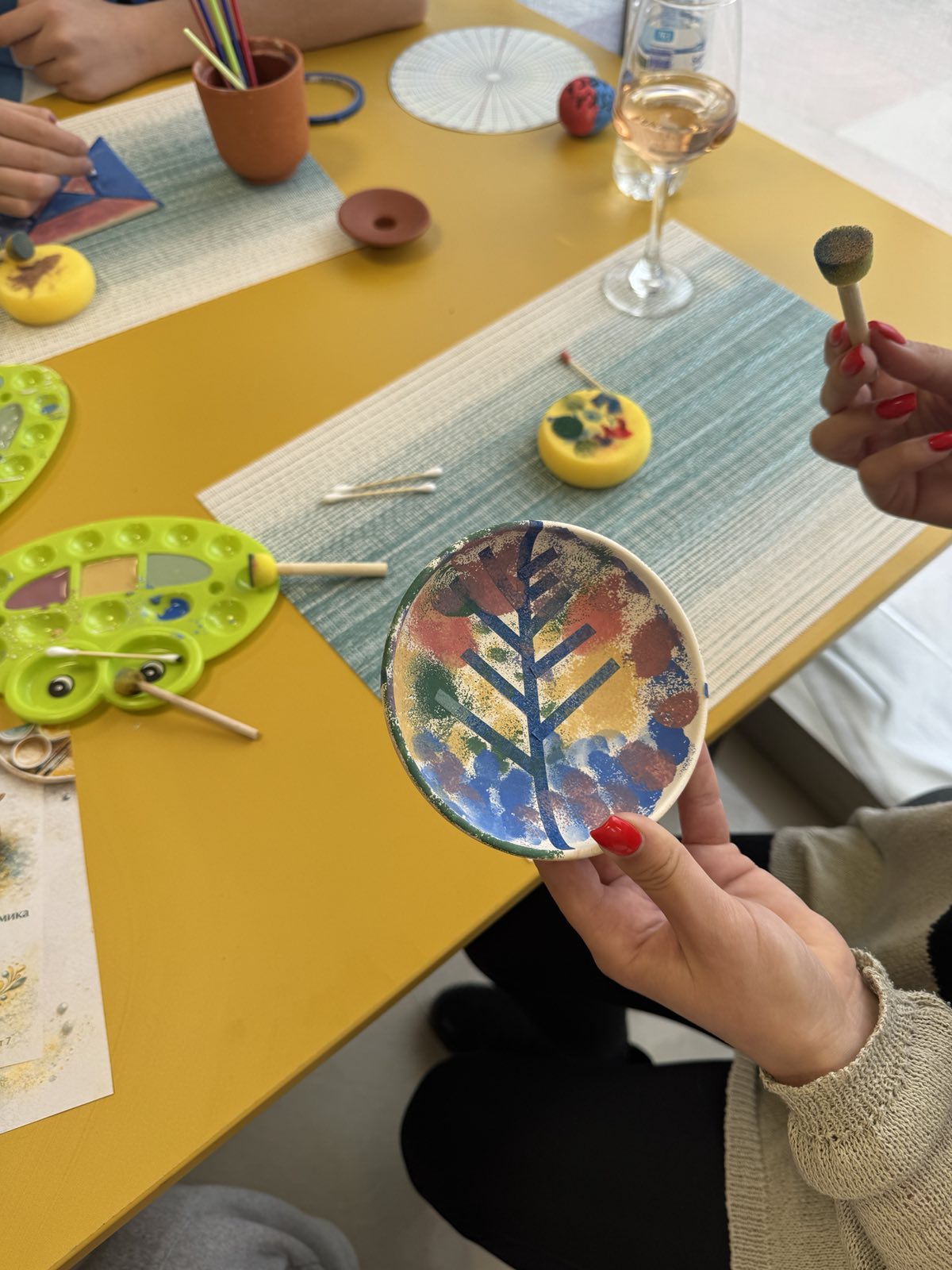 Близък план на палитра с керамични бои, четки и малка купичка